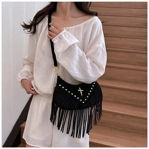 Close-up of black suede crossbody bag with long fringes, rivets and golden cross detail
