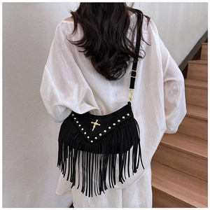 Detail of black suede crossbody bag with gold rivets, cross ornament and long tassels