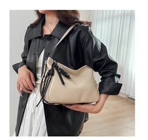 Dettaglio borsa hobo beige con finitura lucida e ciondolo con nappa nera decorativa