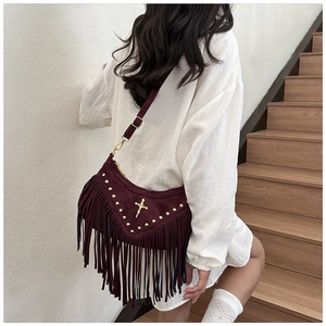 Detail of burgundy suede fringe shoulder bag with golden studs and cross emblem