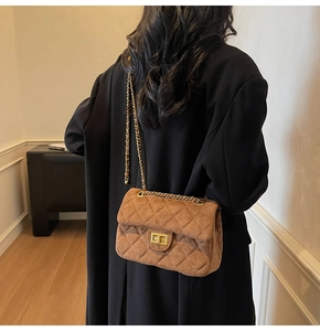 Détail d'un sac bandoulière en velours marron à chaîne dorée porté par un mannequin