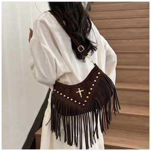 Detail of dark brown suede crossbody bag with gold studs, cross icon, and long fringes