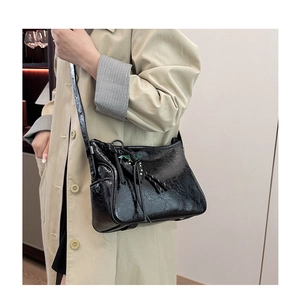 Dettaglio borsa tote nera lucida con nappe decorative e sfondo in trench kaki