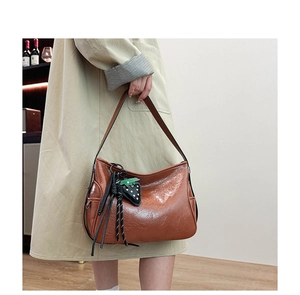 Dettaglio borsa shopper marrone lucida con ciondolo a fragola e nappine su cappotto beige