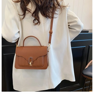 Close-up of brown textured leather crossbody bag featuring a golden oval metal twist lock