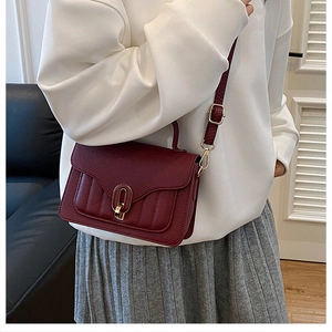 Detail of burgundy lychee grain leather bag featuring a gold buckle and adjustable strap