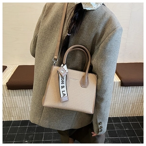Détail du sac à main contrasté beige et marron avec foulard sur un mannequin en costume