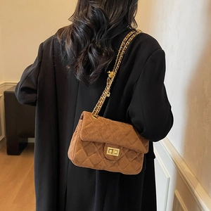 Sac bandoulière en velours marron avec matelassage et chaîne dorée porté par un mannequin