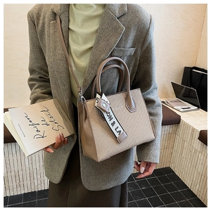 Detail of light brown tote bag with woven texture and decorative letter ribbon strap