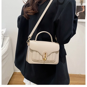 Detail of off-white lychee pattern leather handbag with gold metal clasp on model