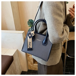 Detail of grey-blue textured tote bag featuring contrast ribbon and brand lettering
