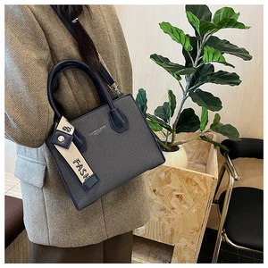 Detail view of navy blue textured crossbody bag with detachable strap and FASH charm