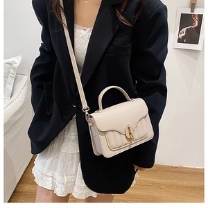 Close-up of cream textured faux leather crossbody bag with oval gold clasp and quilting