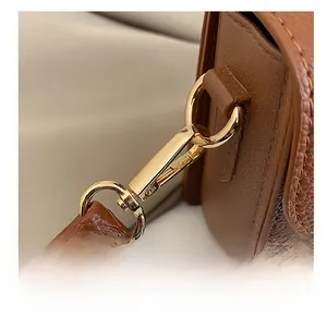 Close-up of golden metal spring hook and wavy stitching on brown leather handbag strap