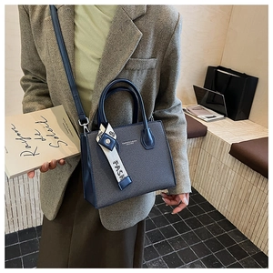 Detail of structured contrast handbag featuring leather handles and chic fashion scarf strap