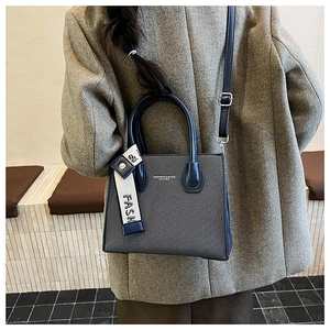 Deep blue trapezoidal handbag with contrast strap worn by a model in a modern interior
