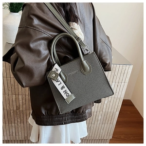 Détail d'un sac à main en cuir vert foncé texturé avec ruban décoratif à lettres chic