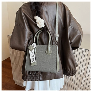 Detail of sage green handbag with twill texture and contrast letter strap on a model