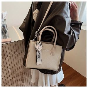 Detail of contrast color handbag with logo strap and textured cream fabric surface