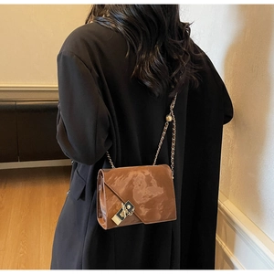 Detail of a brown marble texture crossbody bag with metal chain strap worn by a model