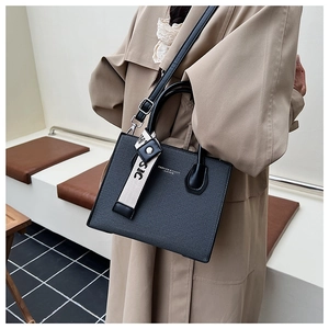 Detail of dark grey woven texture small square bag with decorative classic strap charm