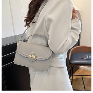 Detail of grey lychee leather crossbody bag featuring a gold round metal twist lock clasp