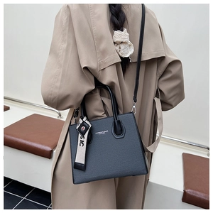 Sac bandoulière en cuir noir minimaliste porté sur un trench-coat beige élégant