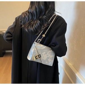 Detail of silver-grey chain bag with marble texture and gold lock on model