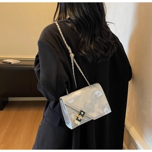 Detail of silver marble crossbody bag with gold chain strap and metallic lock on model