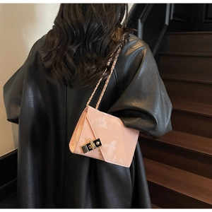 Detail of a light pink patent leather crossbody bag with gold chain strap on a dark coat