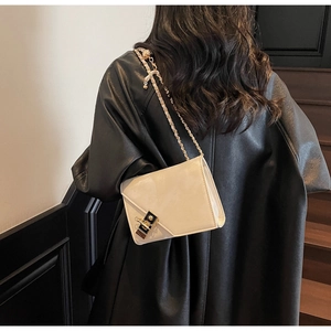 Close-up of white glossy leather handbag with gold chain strap on black leather jacket