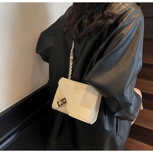 Detail of a creamy white patent leather crossbody bag with a gold chain and metal lock