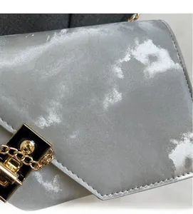 Close-up of golden push-lock clasp and cloud pattern texture on a silver chain bag