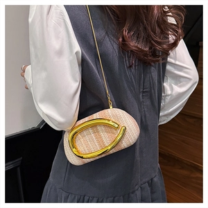 Detail of straw woven crossbody bag with large gold C-shaped metal handle on model