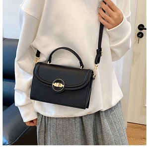 Detailed view of black lychee grain leather handbag with gold hardware and rotary lock