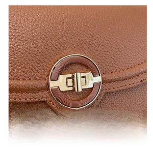Close-up of golden metal round twist lock on brown lychee texture leather crossbody bag