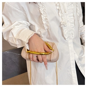 Detail of woven straw bag featuring a gold U-shaped metal handle and slim chain strap