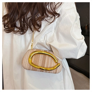Detail of woven straw crossbody bag featuring a large gold C-clasp and metal chain strap