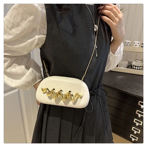 Detail of a beige wave-textured capsule clutch bag with a slim gold metal chain strap