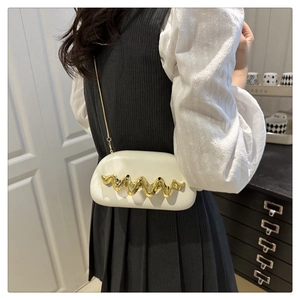 Detail of white cloud clutch with gold wave trim and delicate chain strap worn by model
