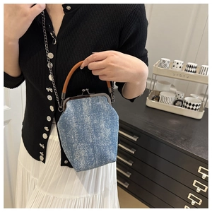 Detail of vintage denim shell bag with silver clasp and leather handle on a model