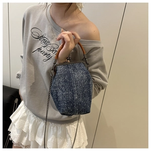 Detail of blue denim kiss-lock shell bag showing star texture and brown leather handle