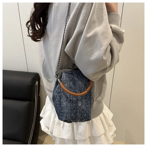 Detail of blue polka dot denim bucket bag with wooden handle and metal kiss-lock closure