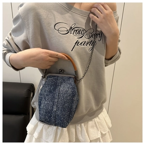 Detail of denim bucket bag showing shell frame, wood handle and metal chain strap