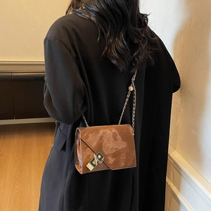 Brown glossy shoulder bag with marble texture and metallic chain strap worn over black coat