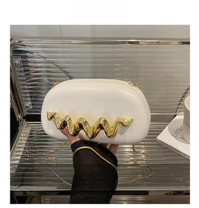 Detail showing white clutch bag with gold wavy metal hardware and fine chain strap
