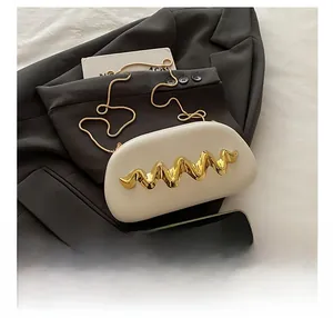 Detail of cream evening bag with wavy gold metal trim on dark grey suit background