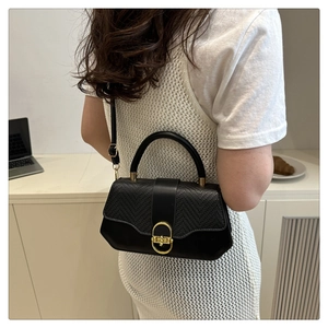 Détail du sac à main noir texturé avec boucle dorée porté par un mannequin dans un café