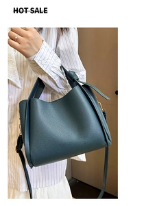 Détail d'un sac seau en cuir grainé vert avec bandoulière et finitions dorées sur modèle