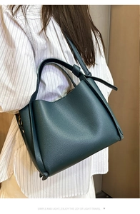 Détail d'un sac seau en cuir grainé vert foncé porté par un mannequin sur mur beige